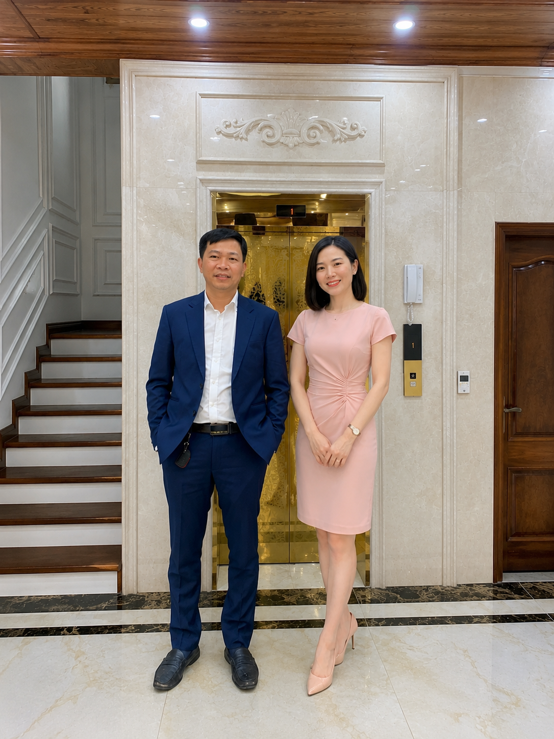 Hai người mặc đồ công sở đứng trước cửa thang máy trong sảnh nhà sang trọng